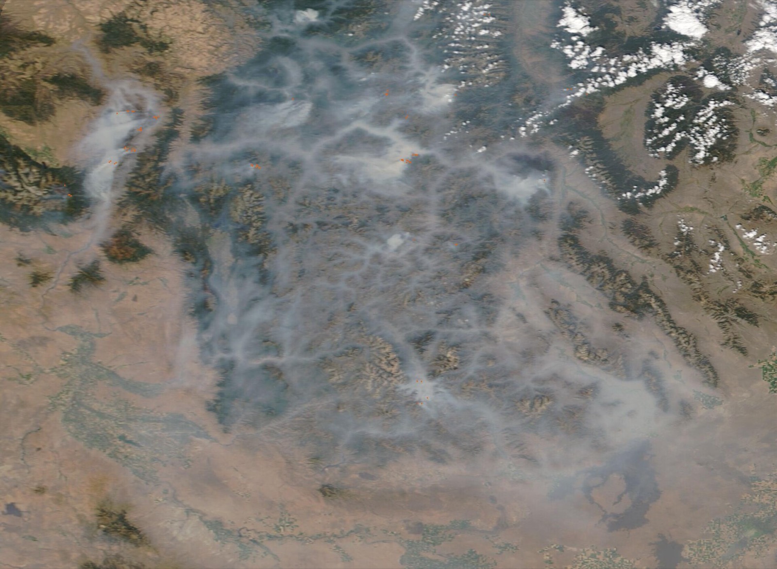 Satellite view of wildfire smoke filling the mountain valleys of central Idaho, with active fire detections marked in red
