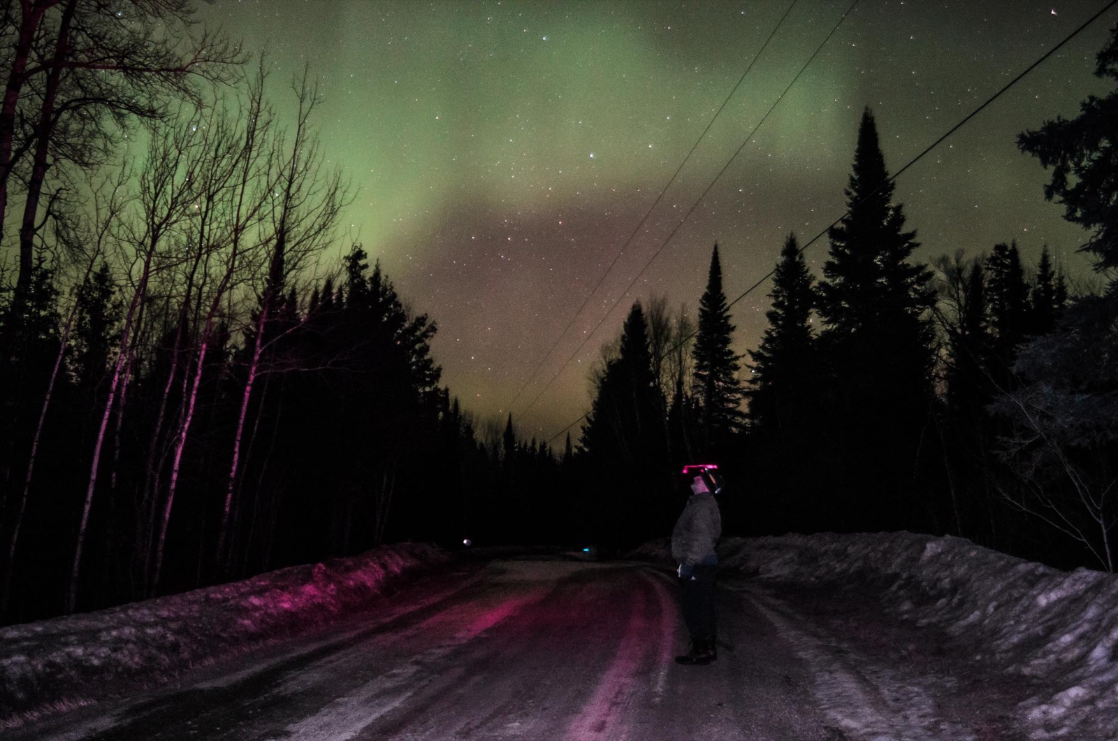 A person photographing the northern lights with a phone on a snowy road