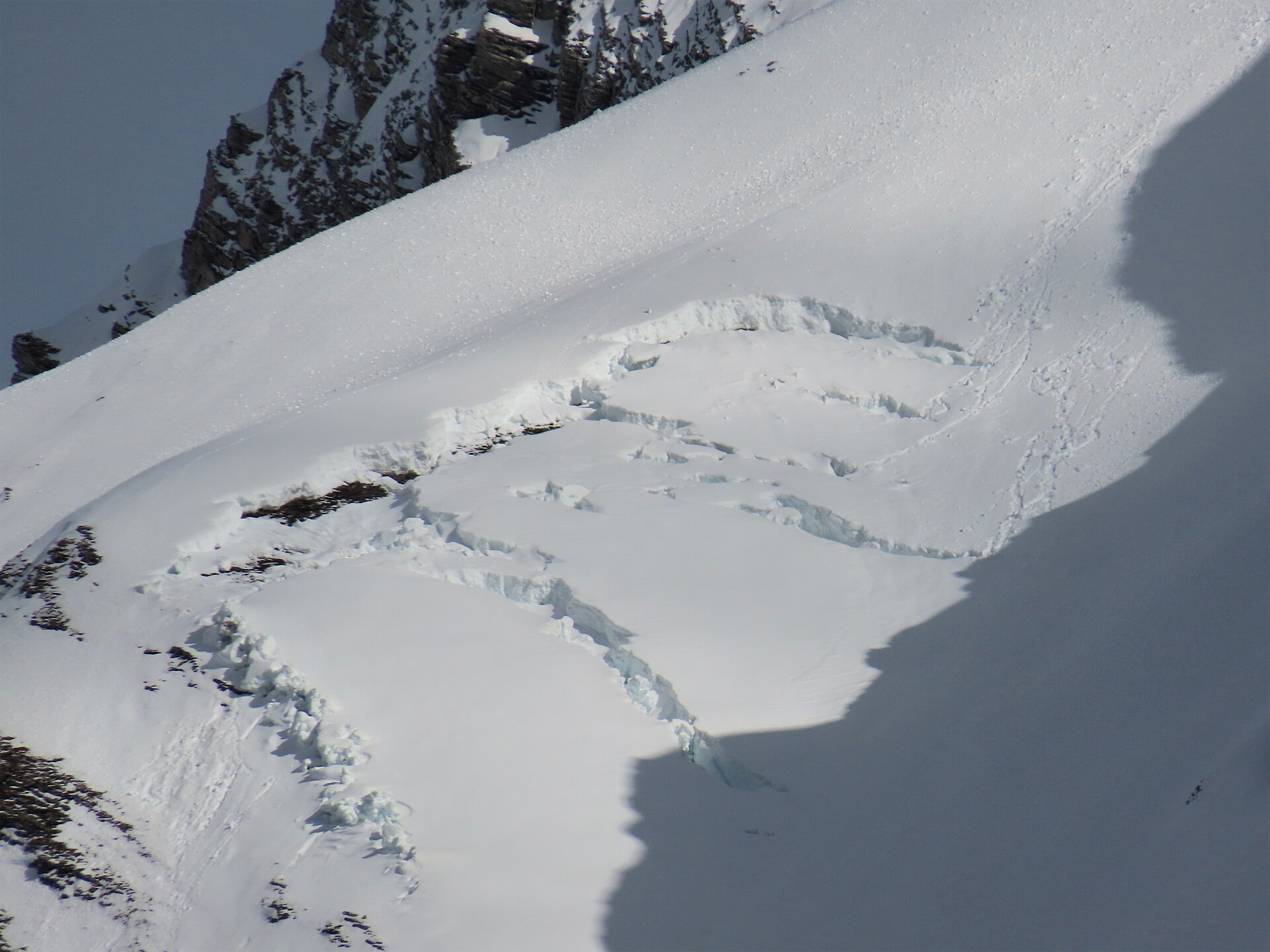 A slab avalanche release on an open snow slope, with several stepped fracture lines cutting across the face and the smooth bed surface exposed below each one