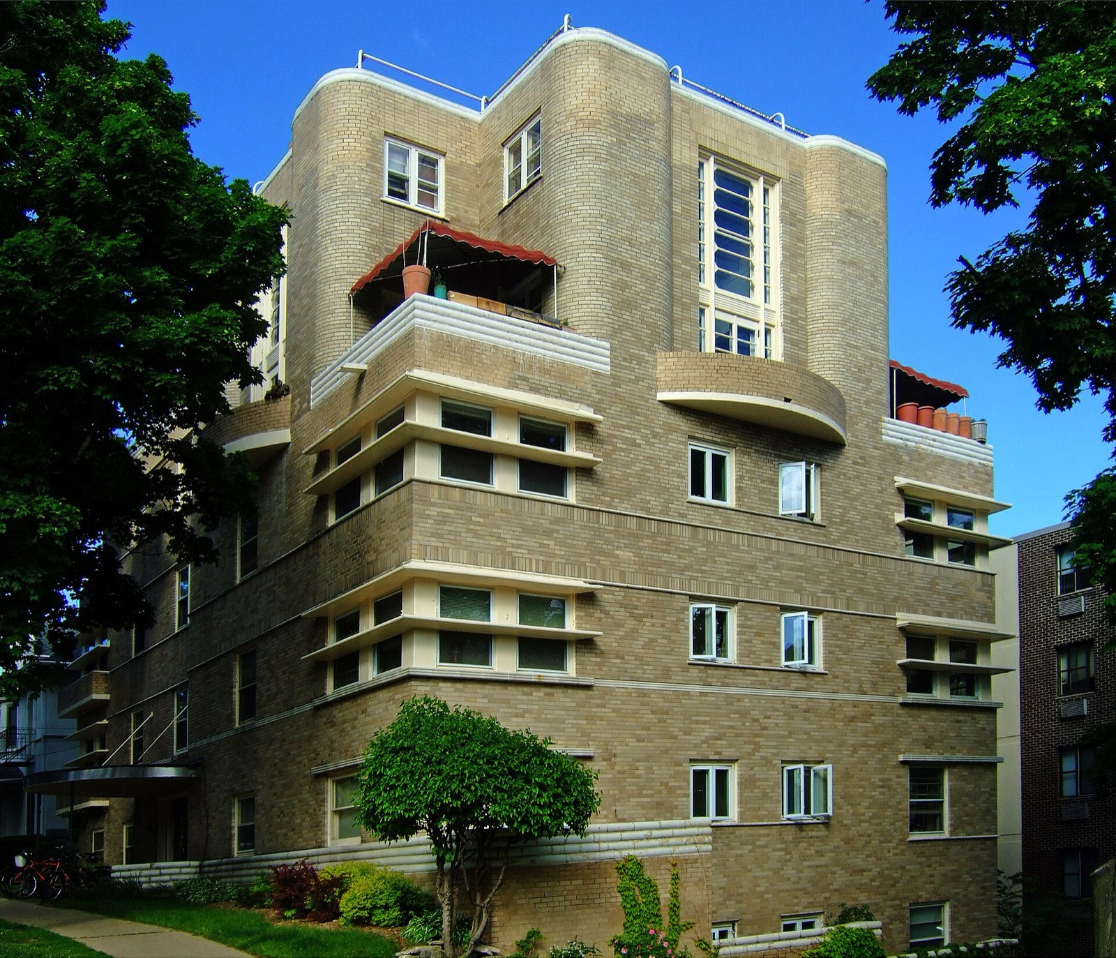 A four storey cream brick apartment building from 1937 in Madison, Wisconsin, with rounded corner bays and projecting window hoods, seen from the corner of the lot.