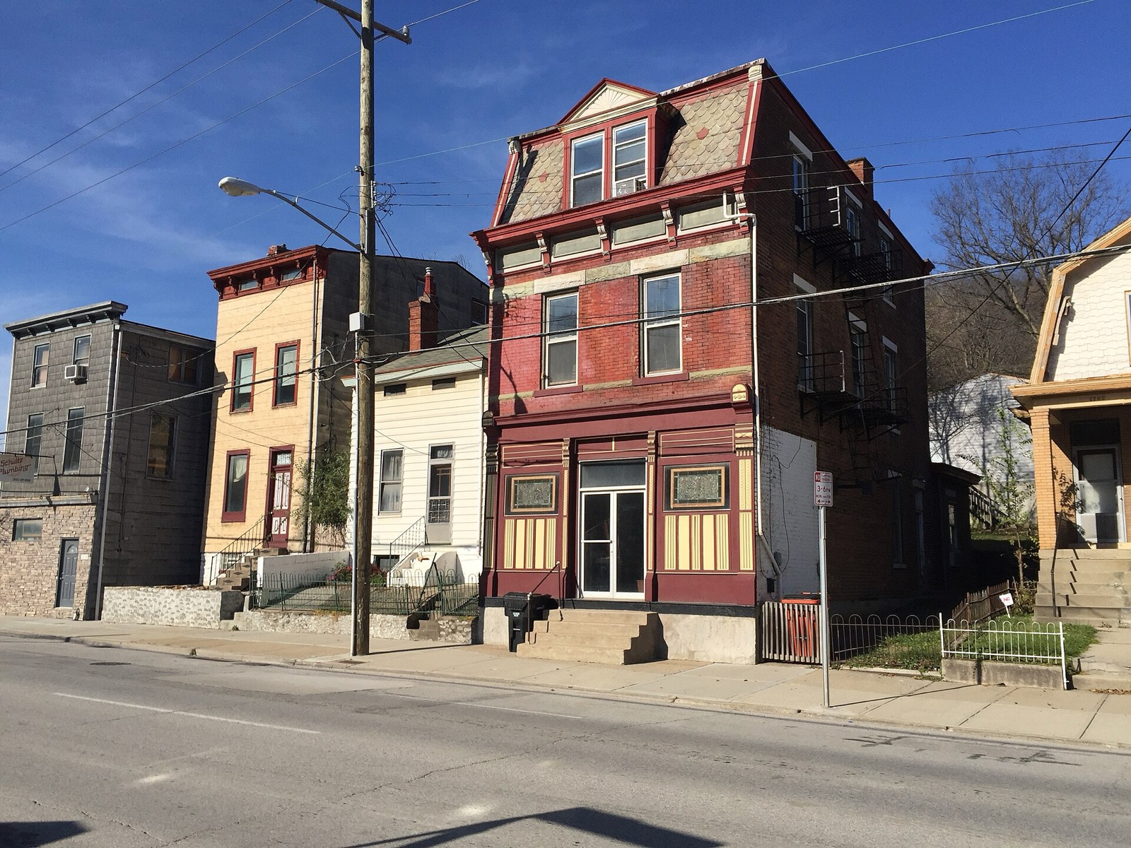 A row of tall nineteenth century brick and frame houses on Queen City Avenue in the South Fairmount neighbourhood of Cincinnati, under a clear sky.