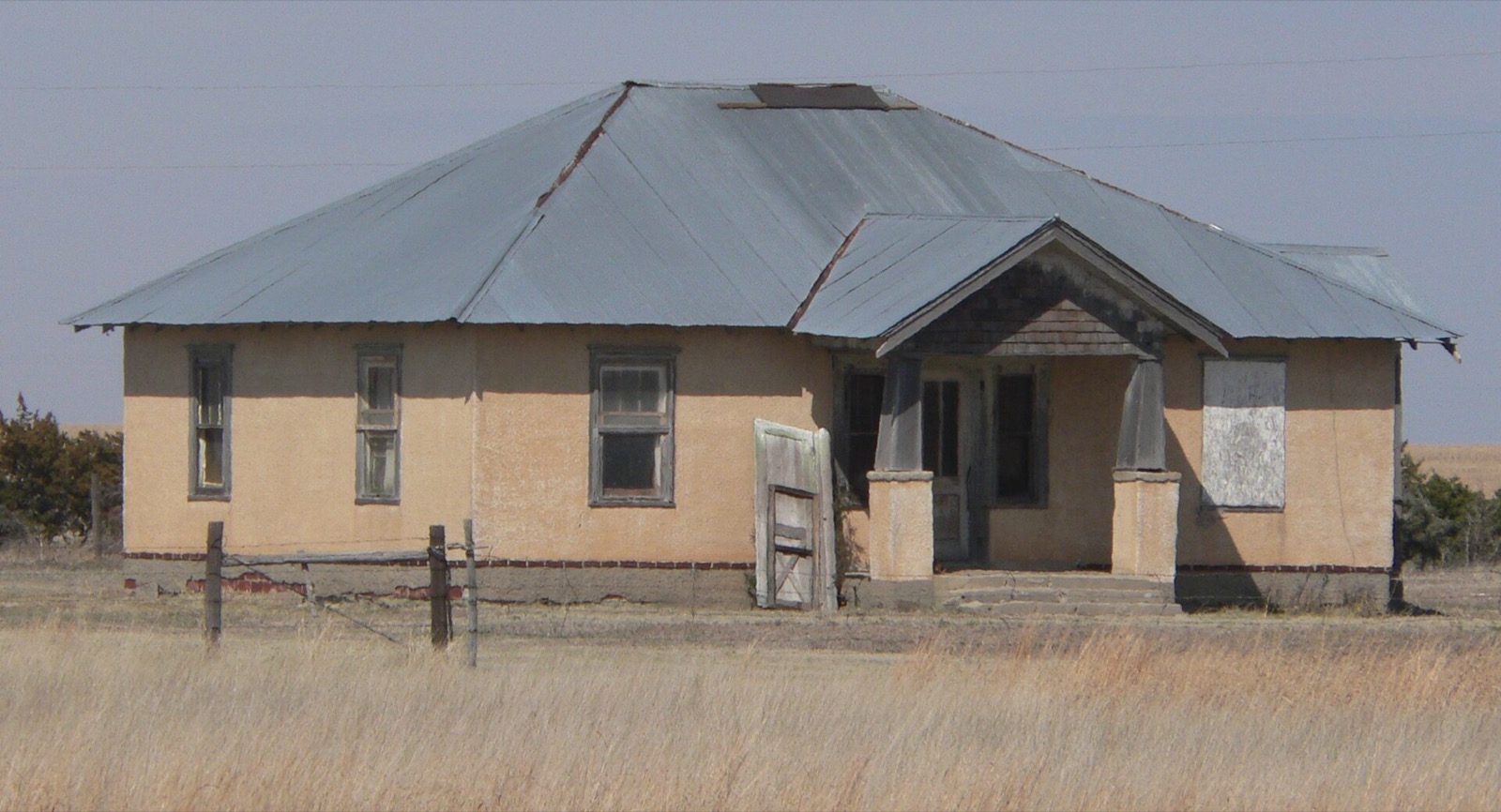 A white two storey farmhouse with a porch standing alone among bare trees on flat open ground in rural Lane County, Kansas.