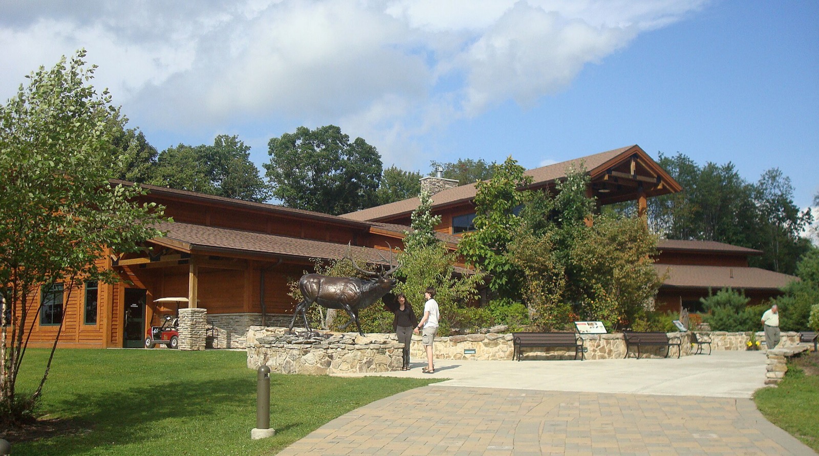 A large timber and stone visitor centre building with a bronze elk sculpture on a stone wall in front of it