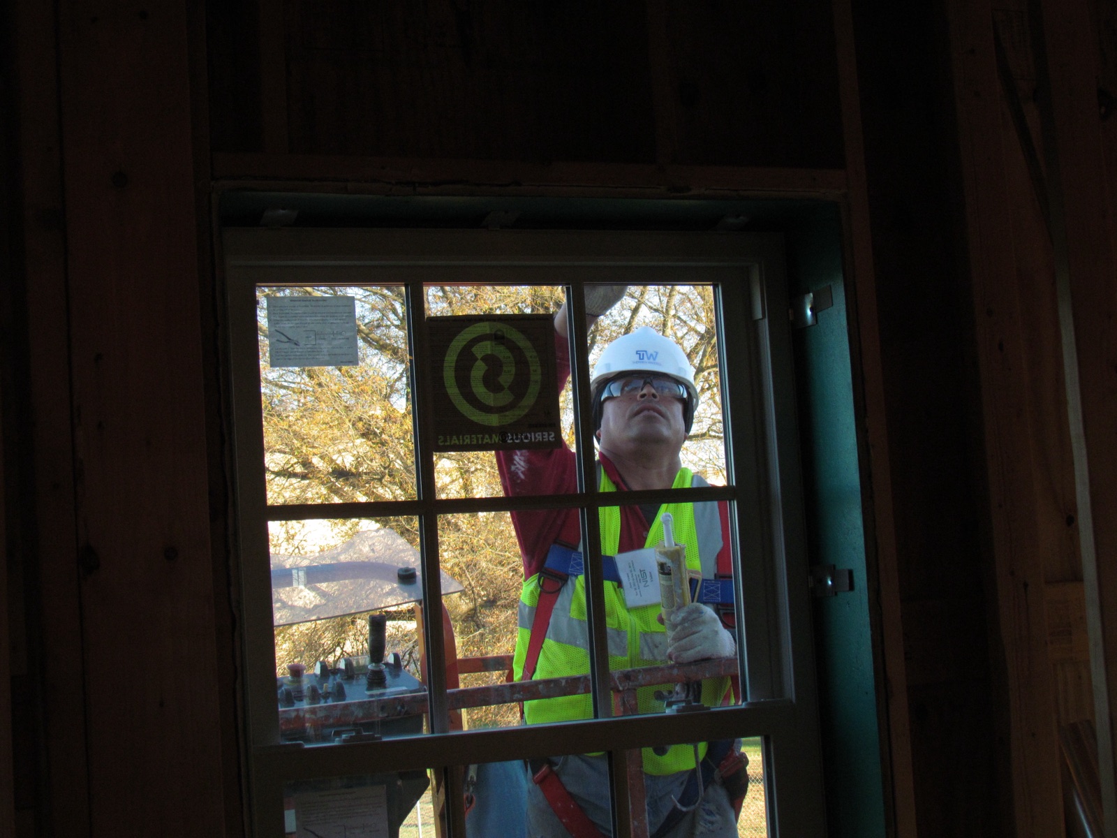 A worker on a ladder applying caulk around the exterior trim of a house window