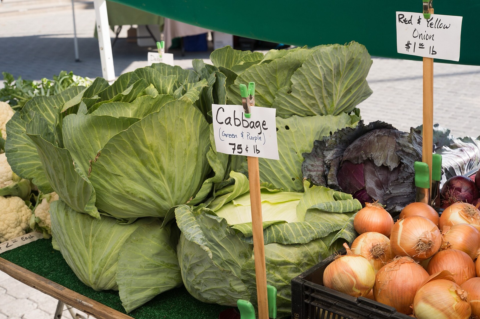 Cabbages, cauliflower and yellow onions on a market table with handwritten price cards