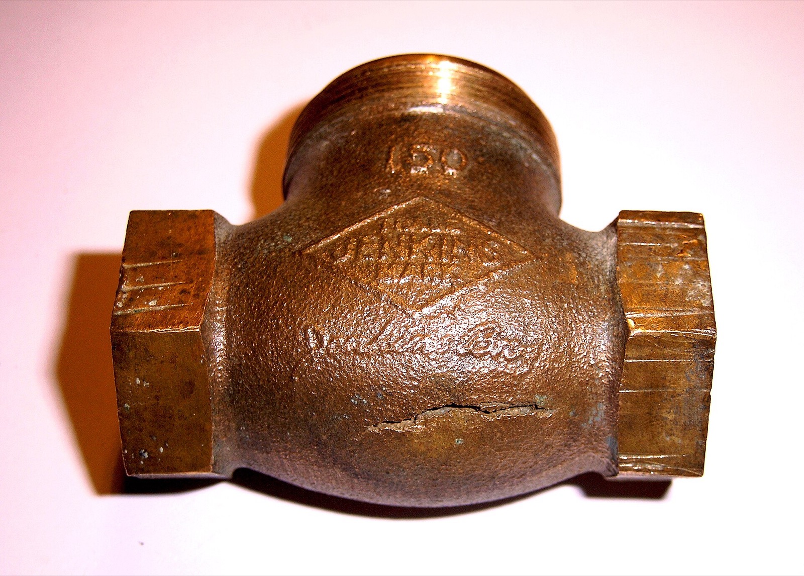 A brass shutoff valve body photographed against a plain background, with a long clean split running along the underside of the casting
