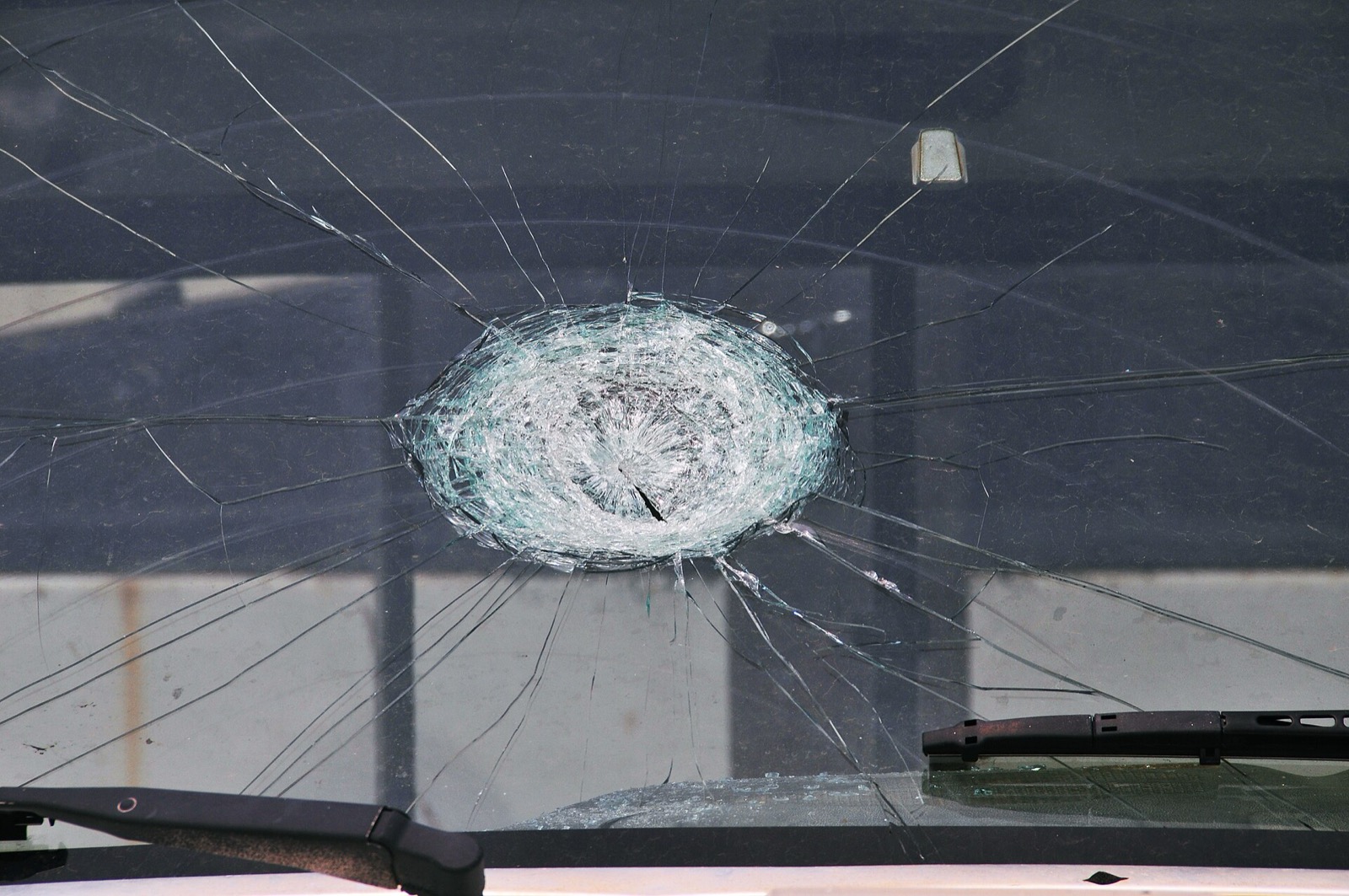 A truck windshield with a large circular impact crater from a hailstone and long cracks radiating across the glass