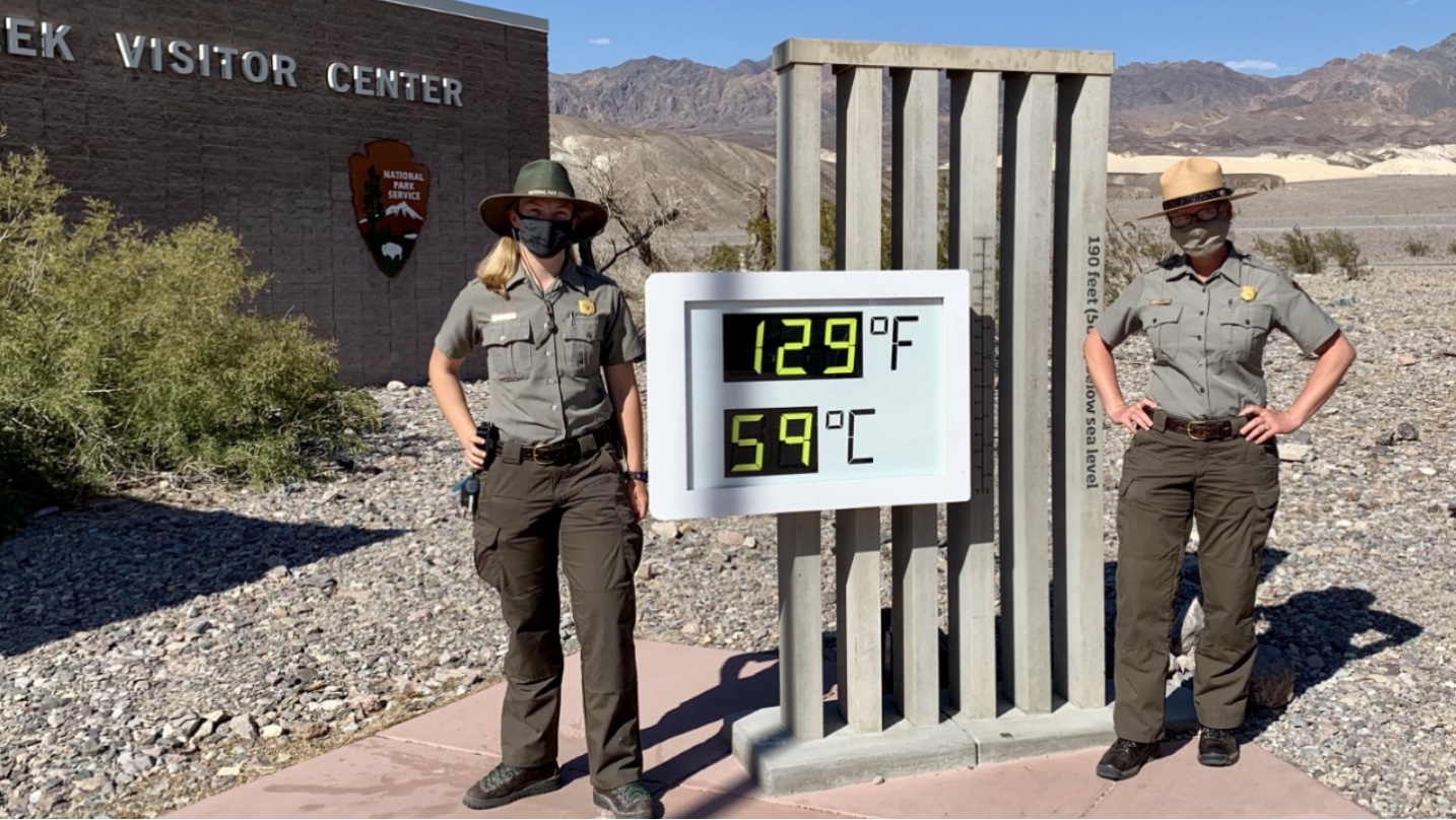 National Park Service rangers beside the Furnace Creek visitor center sign in Death Valley reading 129 degrees Fahrenheit