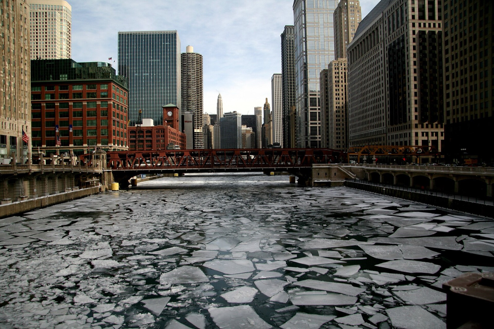 Broken ice floes covering the Chicago River between downtown buildings, with the Wells Street Bridge behind