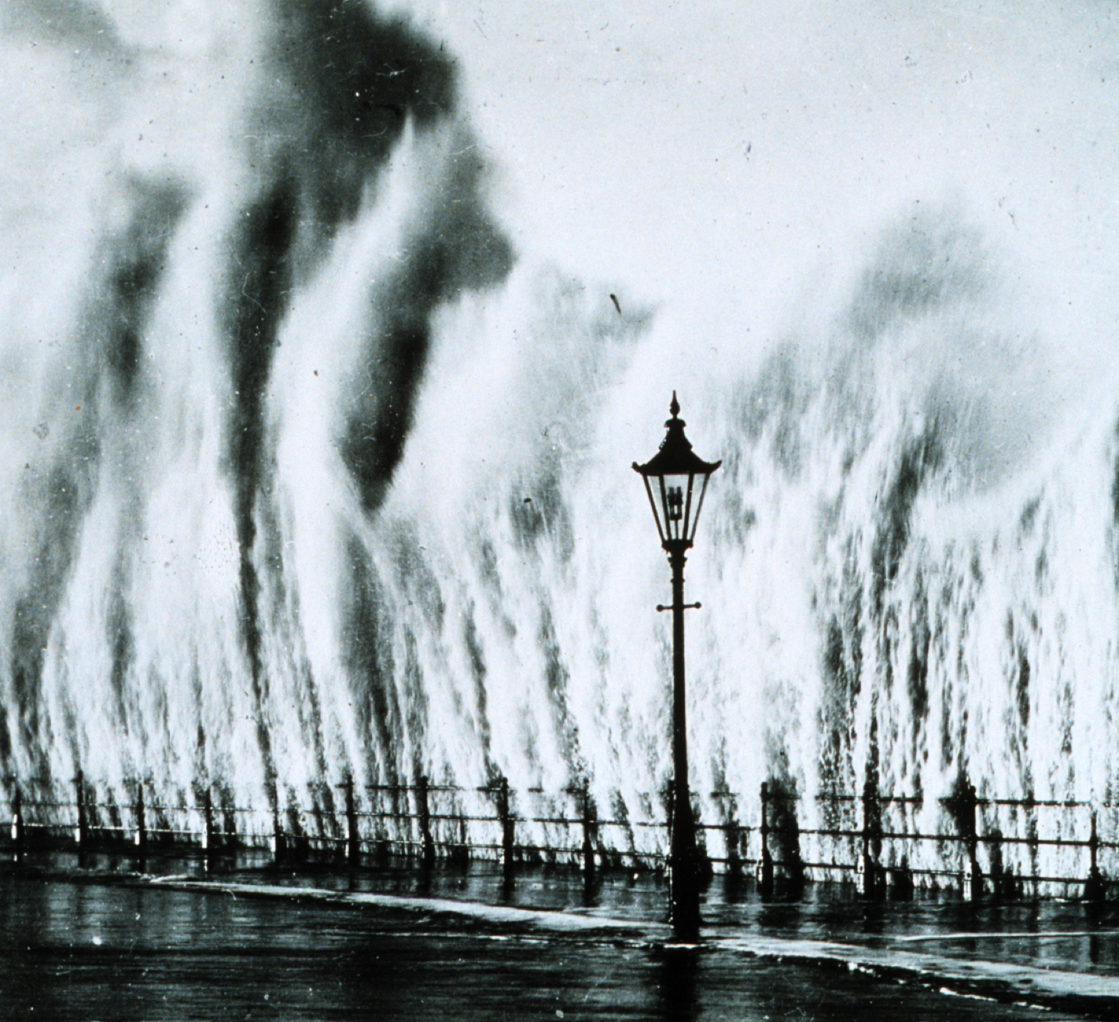 A wave from the 1938 New England hurricane storm surge exploding against a seawall, towering over a lamppost