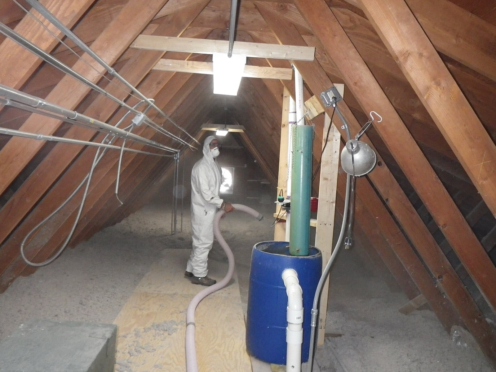 Loose cellulose insulation being blown across an attic floor by a worker in coveralls