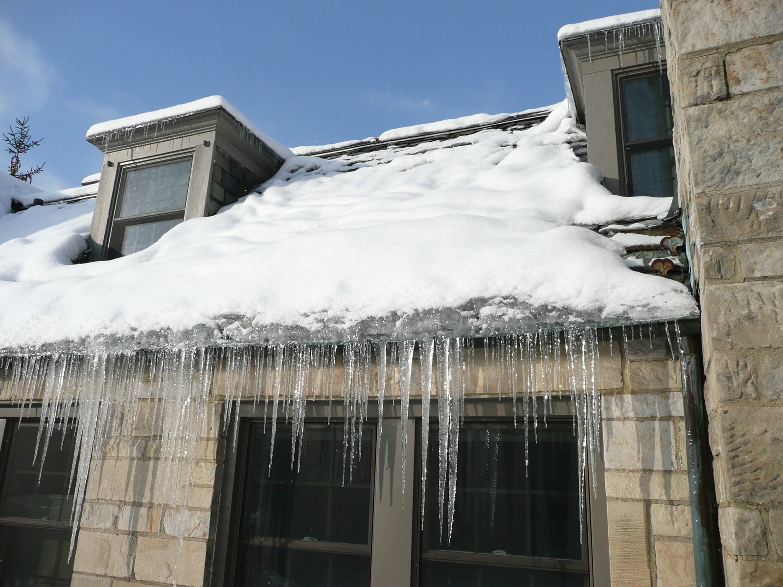 Ice built up in a thick ridge at the eave of a snow-covered slate roof, with icicles hanging below