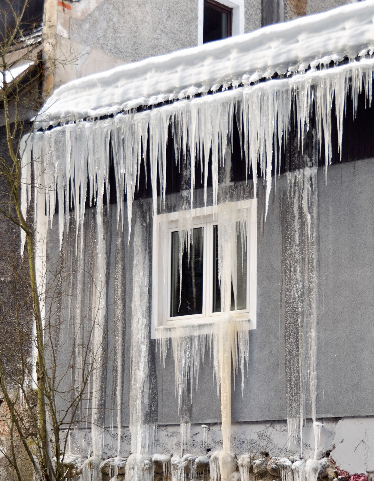 Meltwater from a roof eave that has run into a wall and refrozen in sheets down the facade around a window