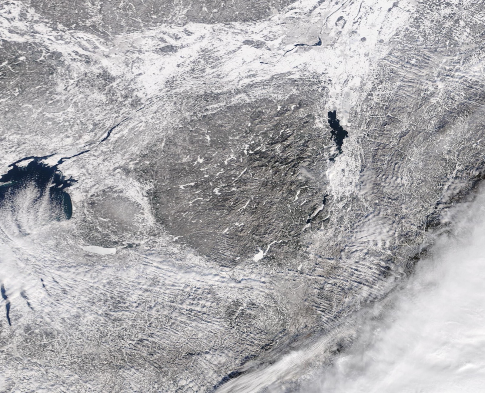 Satellite view of snow covered northern New York in mid January, with the darker Adirondack uplands in the centre and the long narrow shape of Lake Champlain running dark and open down the right hand side