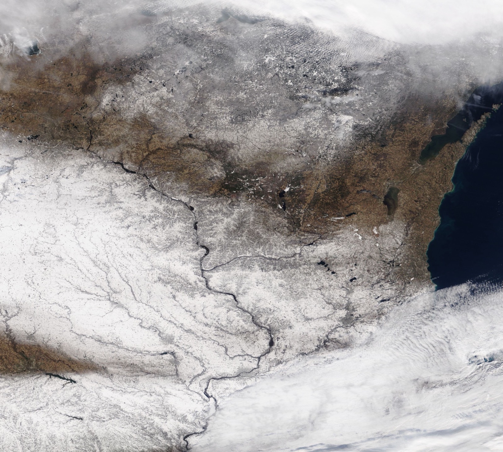 Satellite view of snow across Iowa and southern Minnesota in mid November, with the Mississippi River threading through it, bare brown ground to the northeast and Lake Michigan dark at the right edge