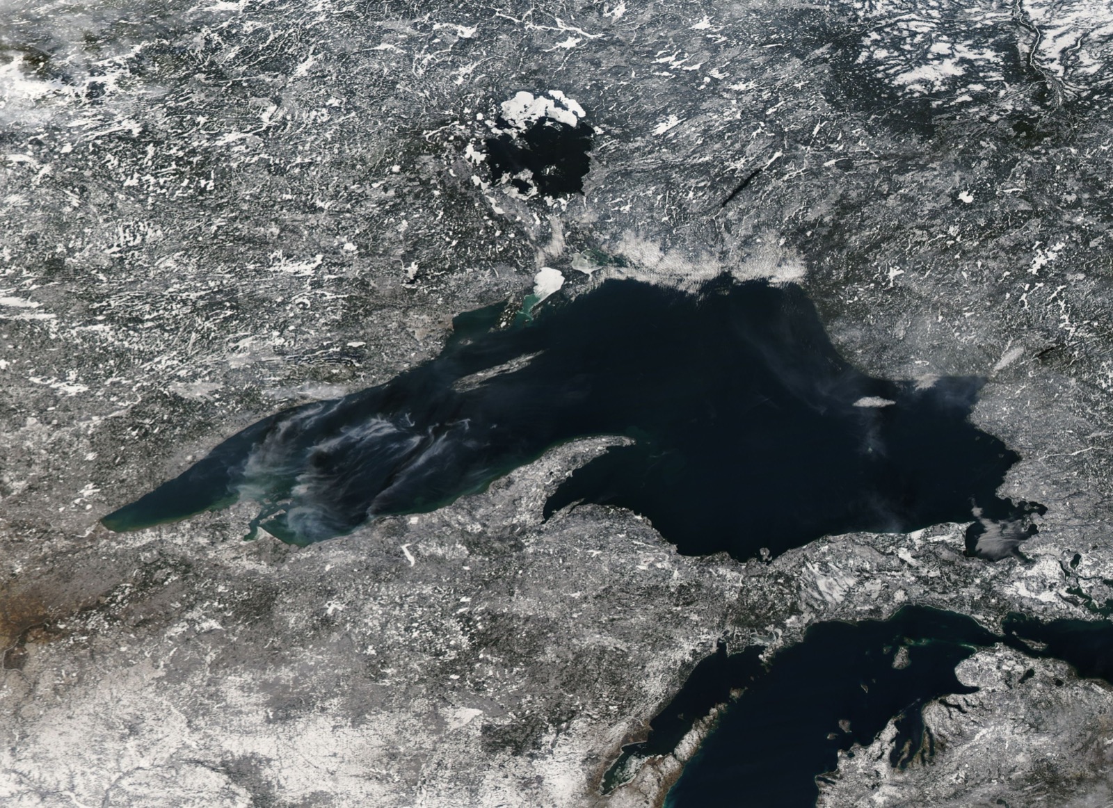 Satellite view of Lake Superior in mid December with the surrounding land under snow, the open lake dark, and pale new ice showing in the shallow western bays