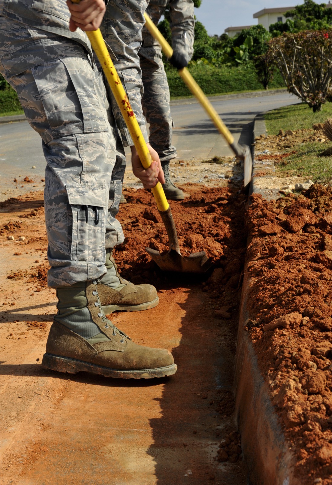 A crew backfilling a trench along a curb after replacing a water pipe
