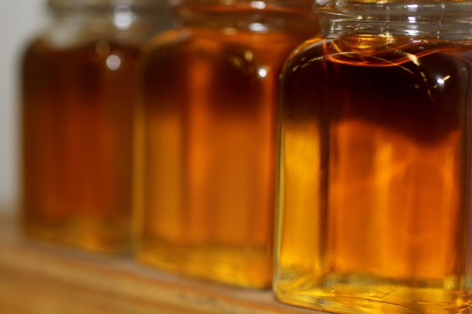 Glass jars of finished maple syrup in a row, ranging from light amber to dark