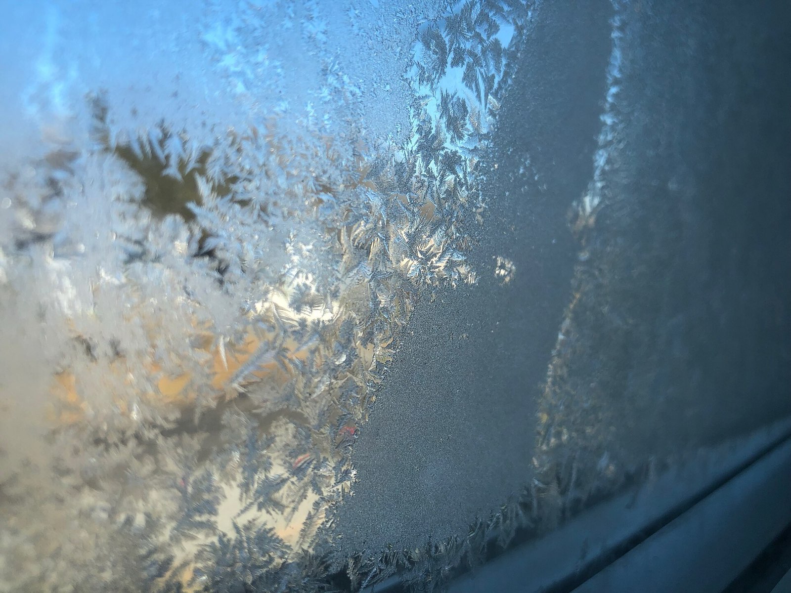 Ice crystals covering the inside surface of a window pane on a cold winter morning, with the view outside barely visible through the frost