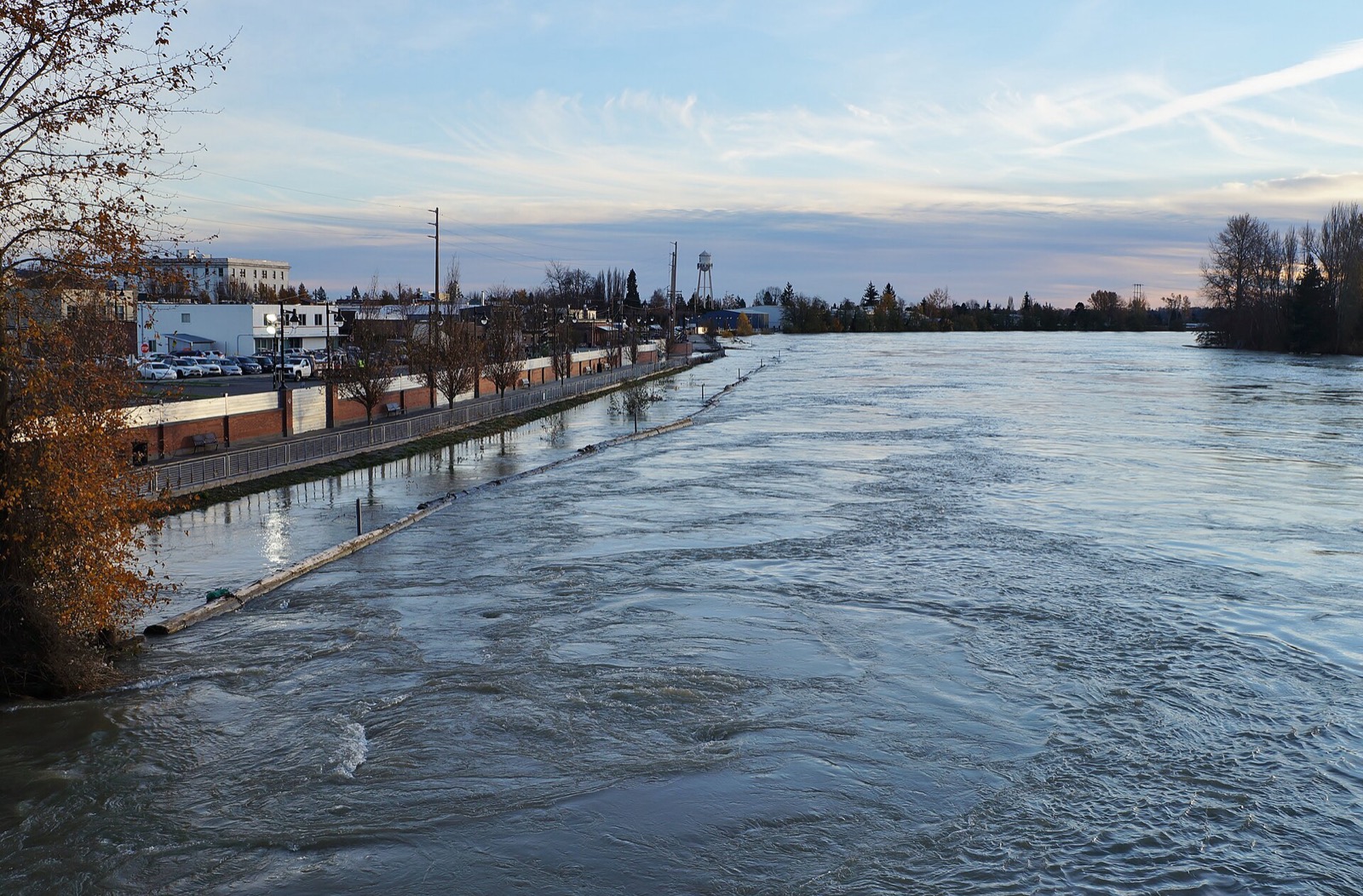 A river running brim full against a downtown floodwall walkway in late fall light
