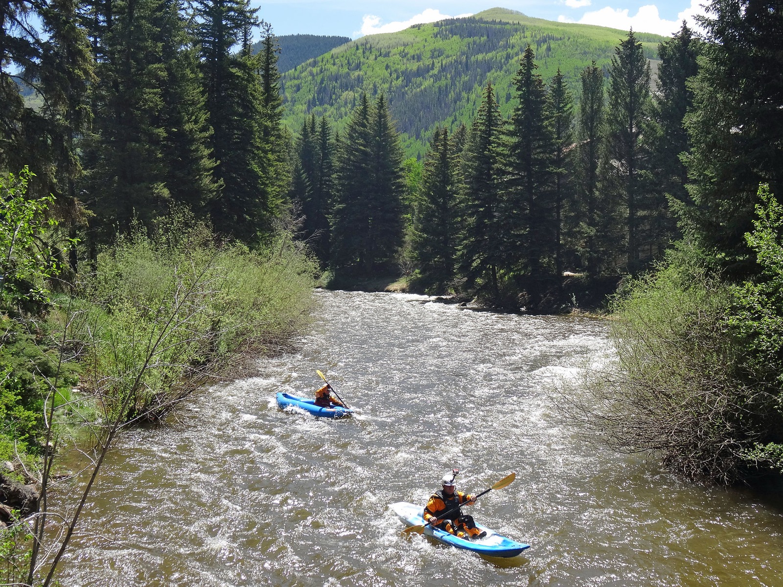 Two kayakers riding a small creek running high and fast between wooded banks