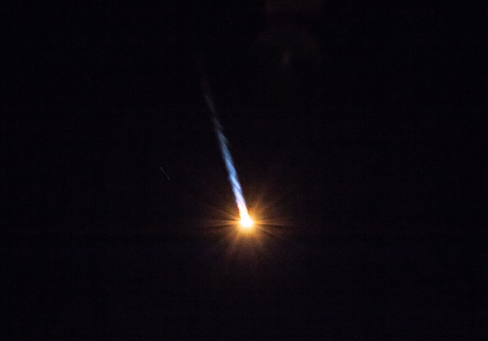 A bright orange flame with a thin blue and white exhaust trail streaking down through a black night sky