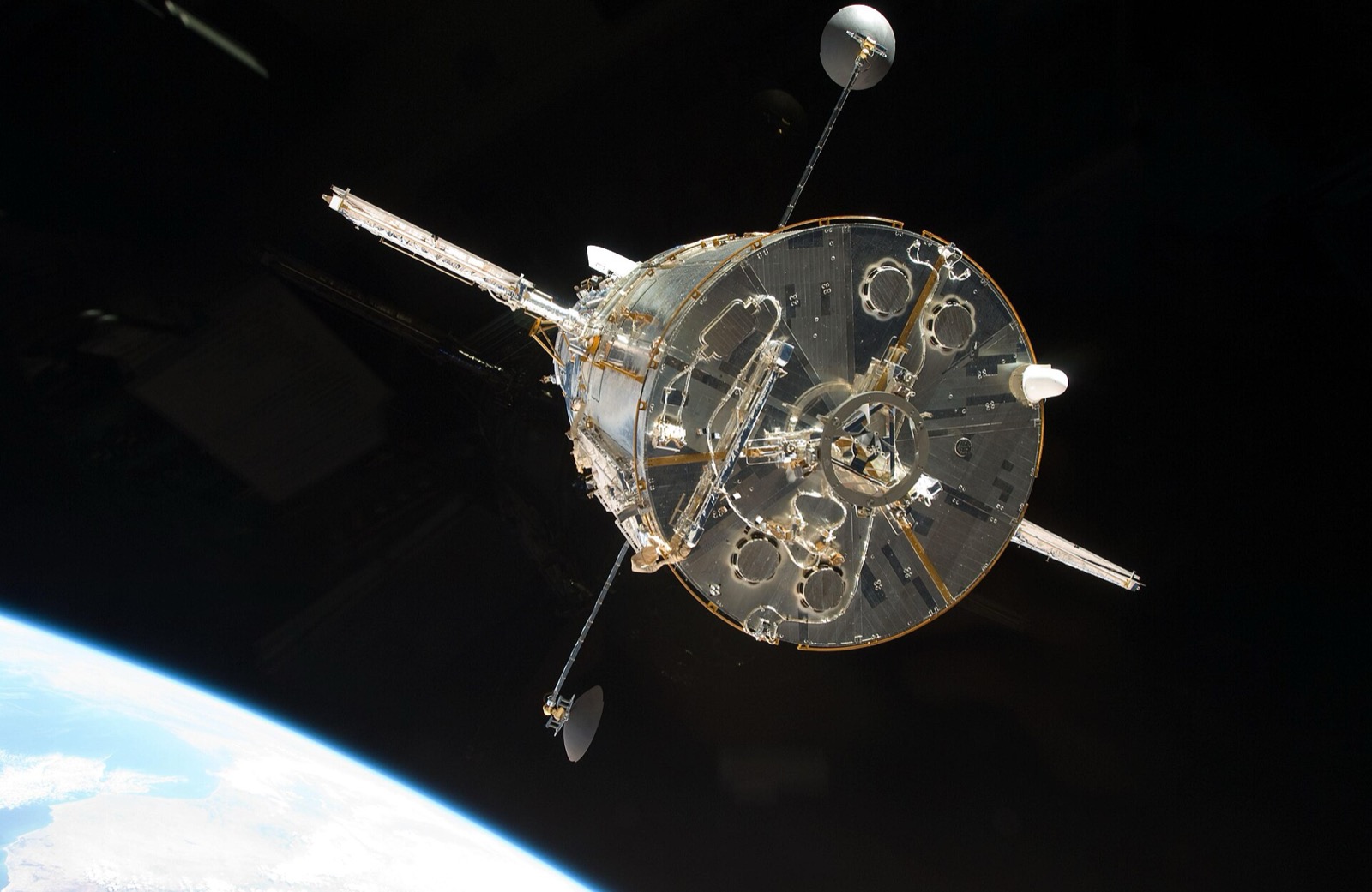 The Hubble Space Telescope, a silver cylinder with antennas and folded solar arrays, floating against black space with the blue curve of Earth at the lower left