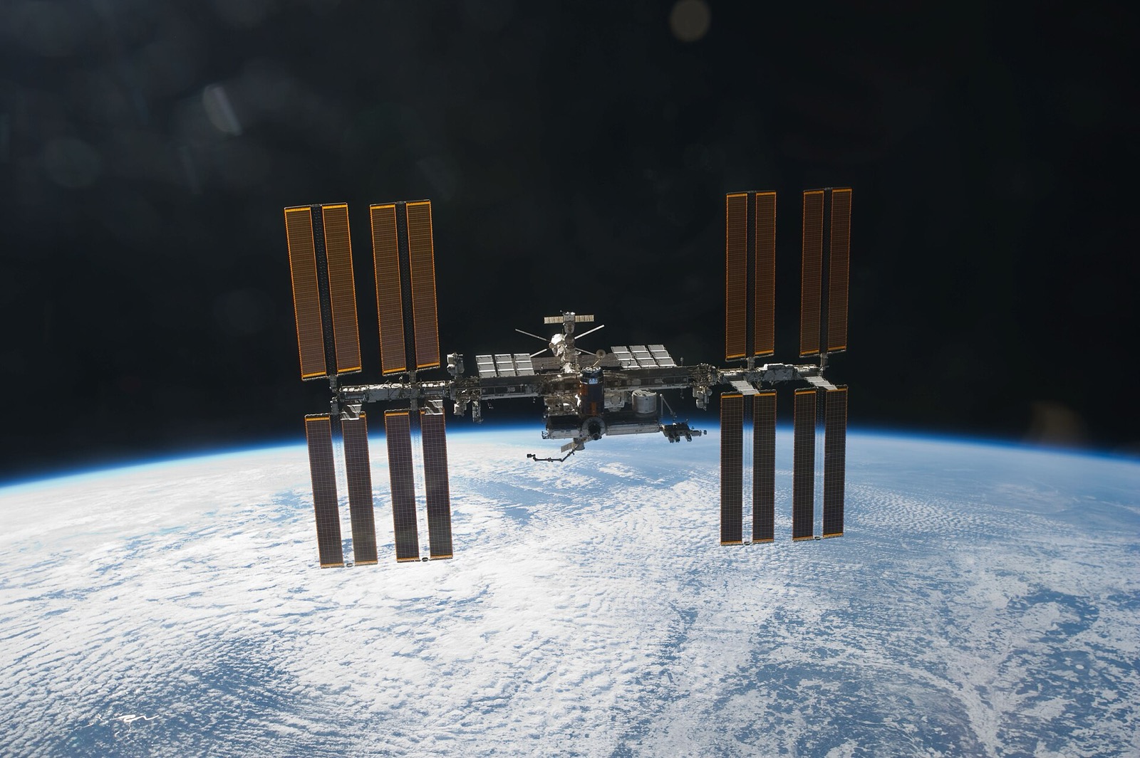 The International Space Station seen from a departing space shuttle, its eight long gold solar wings spread above a white, cloud covered Earth and a black sky