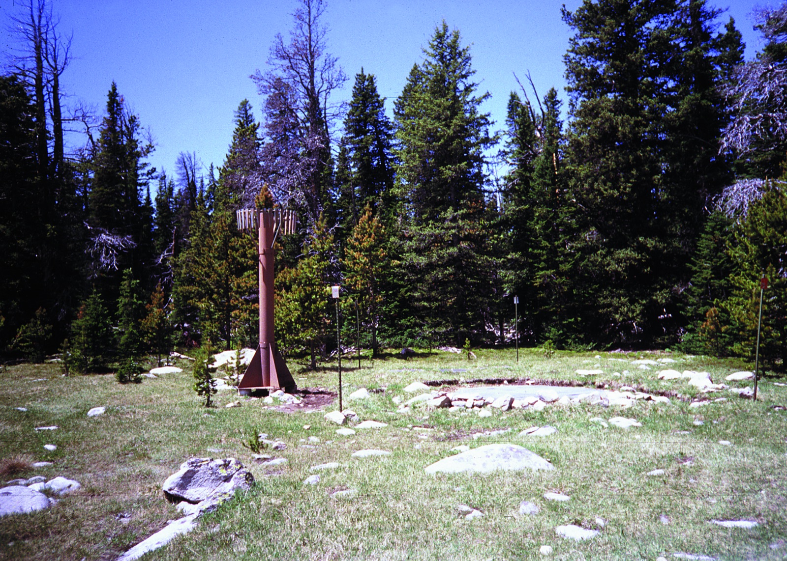 A SNOTEL snow measuring site in a forest clearing in Montana, with its precipitation gauge and snow pillow pad