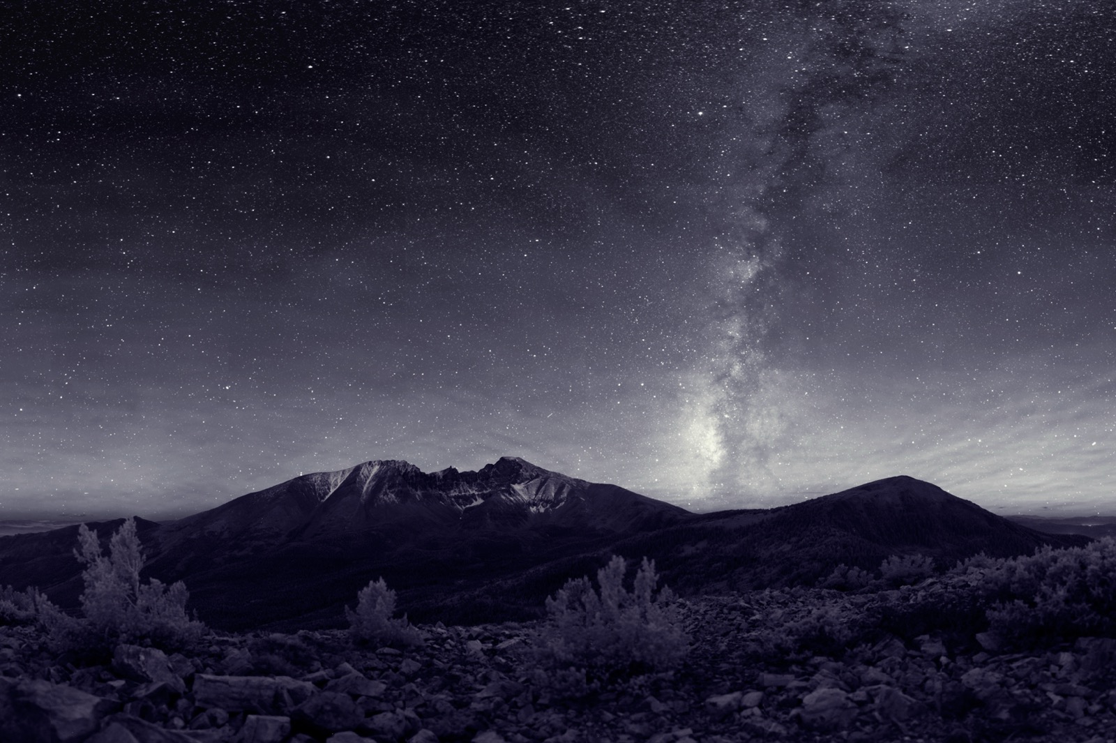 The Milky Way core arching over a dark desert horizon on a moonless night