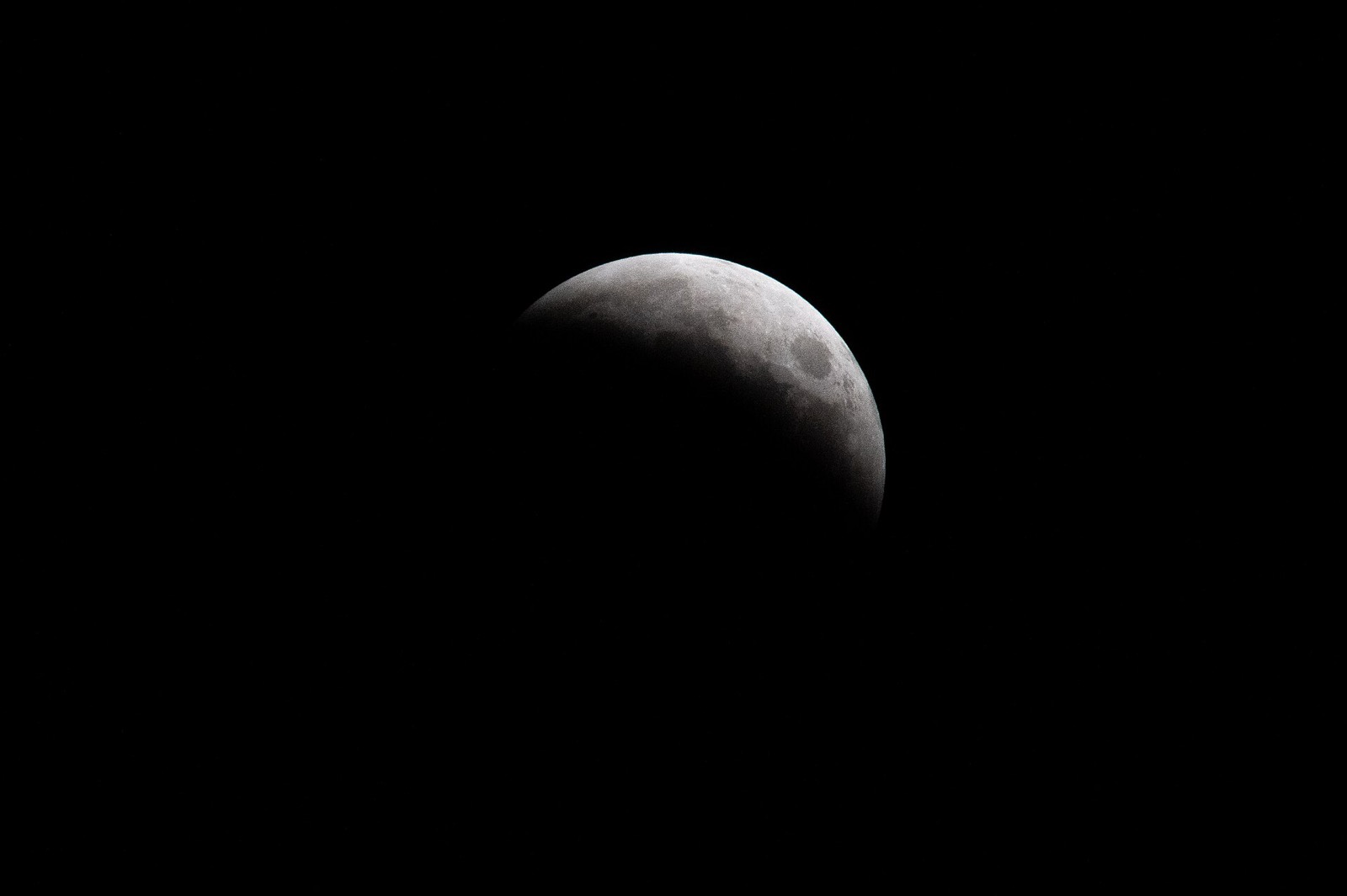 A partially eclipsed moon against a black sky, with the Earth's shadow taking a curved bite out of its lower left