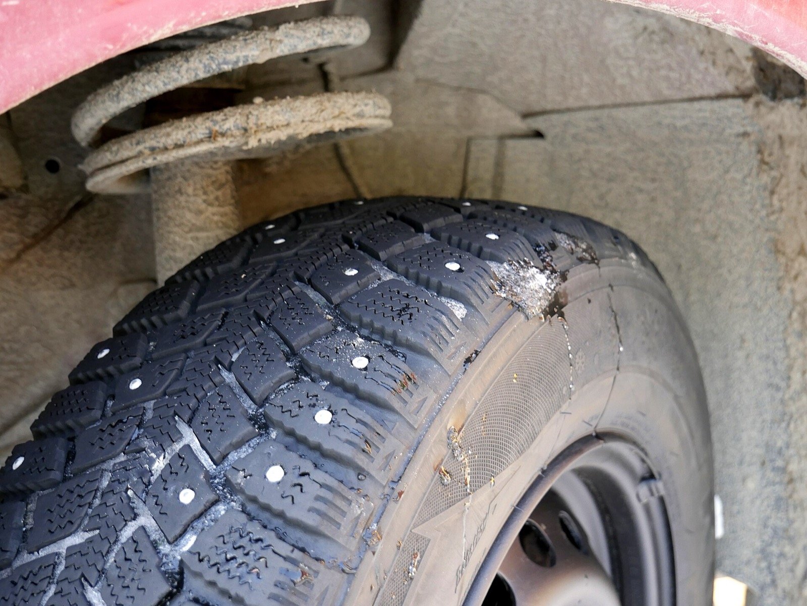 Close view of a winter tire tread set with rows of small metal studs, mounted on a red car