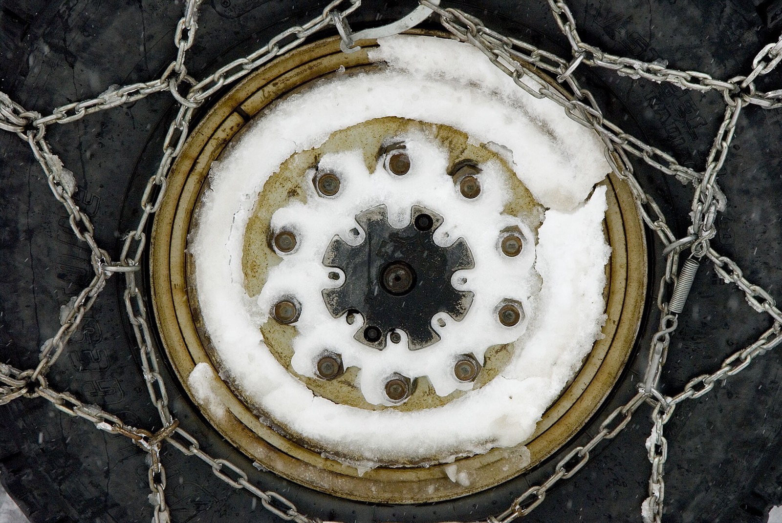 Tire chains wrapped across a truck tire, with snow packed around the wheel hub