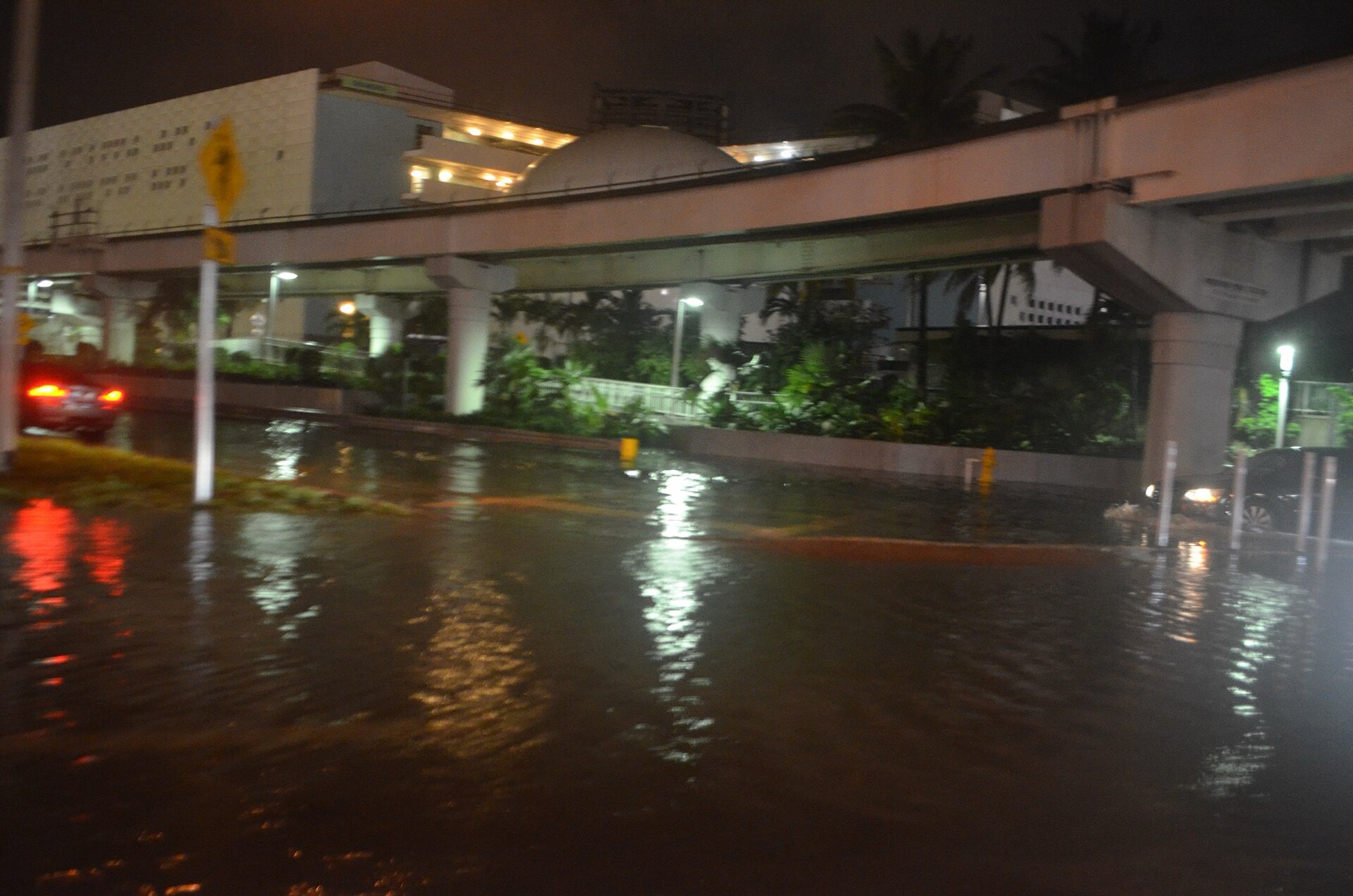 A city street in Miami flooded at night by tidal water during a king tide, with headlights reflecting off the water