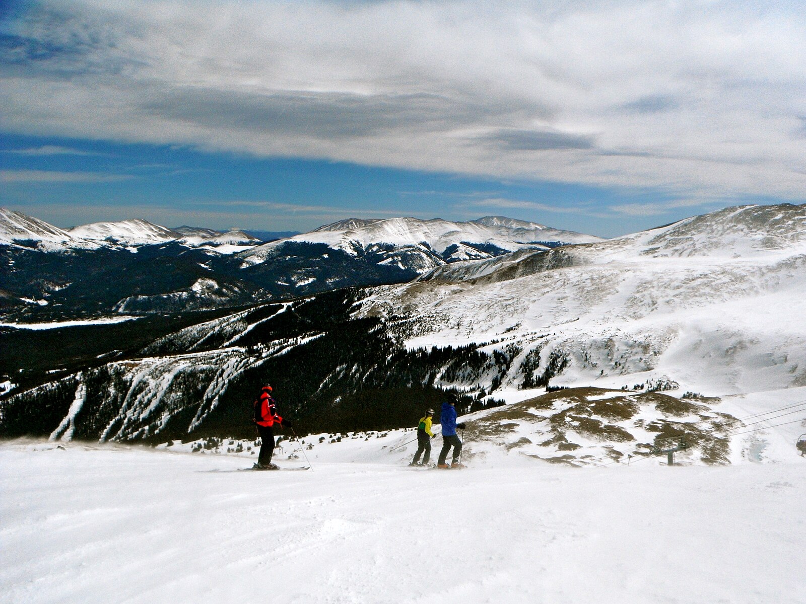 Skiers on a high open snow slope at Breckenridge, Colorado, under strong sun, with snowy ridges to the horizon