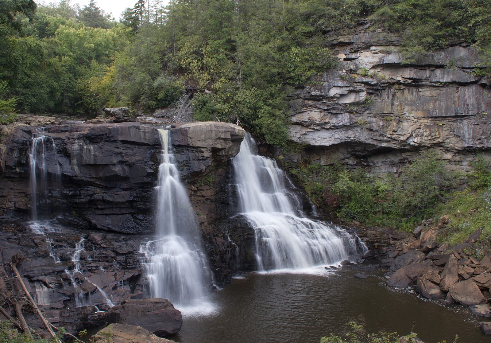 A tiered waterfall dropping through a wooded rock gorge