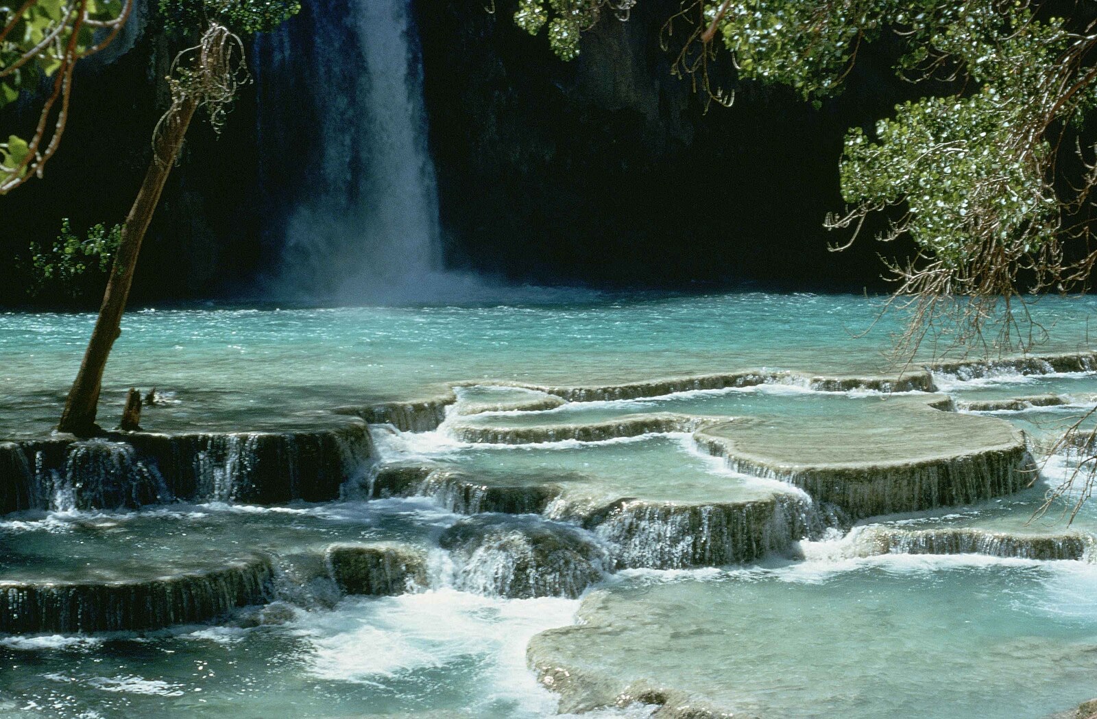 Blue green travertine terraces below Havasu Falls with the falls dropping into the pool behind