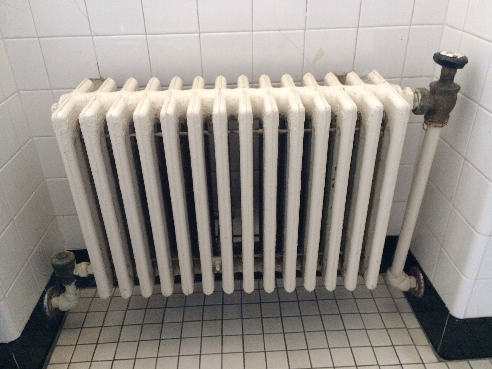 A cast-iron steam radiator under a window in a room with wooden floorboards